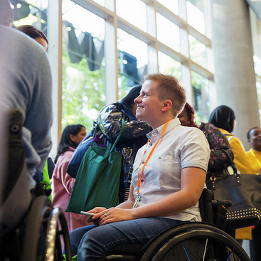 A wheelchair user admist a crowd of people wearing a conference tag.