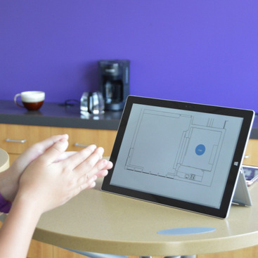 A person claps in front of a tablet interface that visaulizes the clapping sound using a pulsating bubble. The bubble is placed inside one of the rooms in a floorplan view of the location.