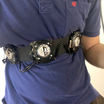 Our haptic belt VR sound feedback prototype consisting of 8 rounded 4-inch grey actuators attached on a velcro, worn across the chest of a user wearing a blue t-shirt.