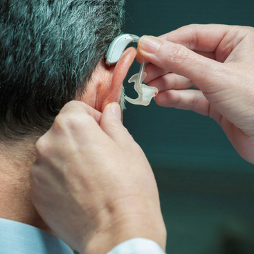 A person's face from the back showing him donning a hearing aid.